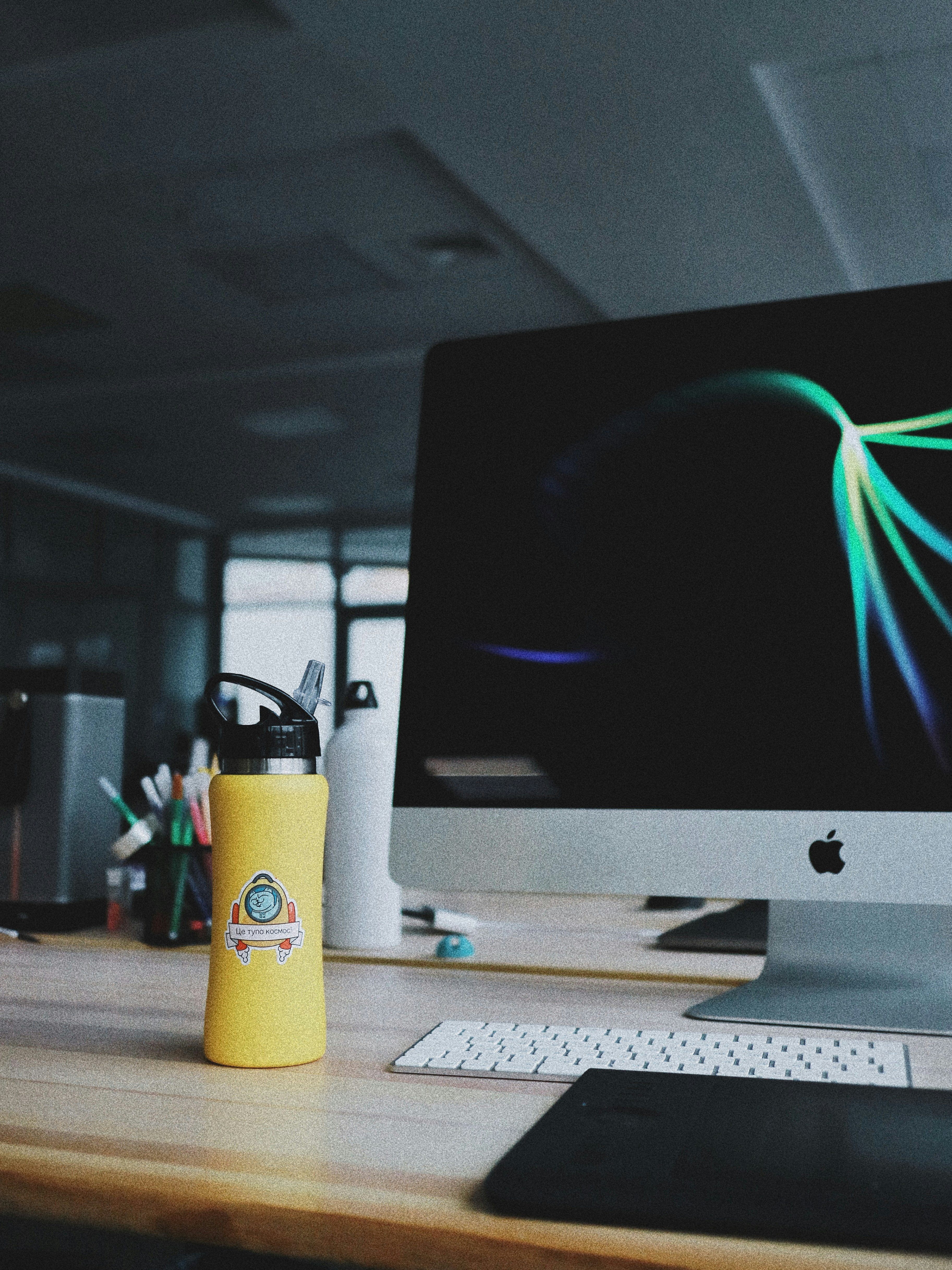 powered on silver iMac beside yellow tumbler